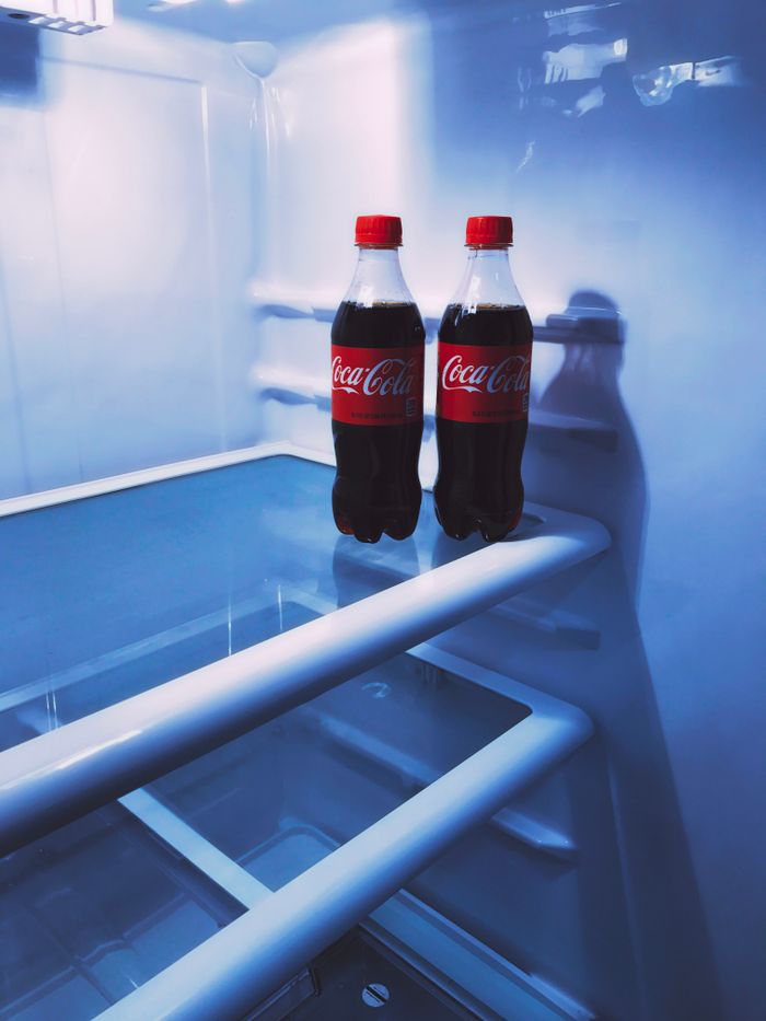Two Coca-Cola bottles inside a refrigerator, showcasing the cool refreshing drink.