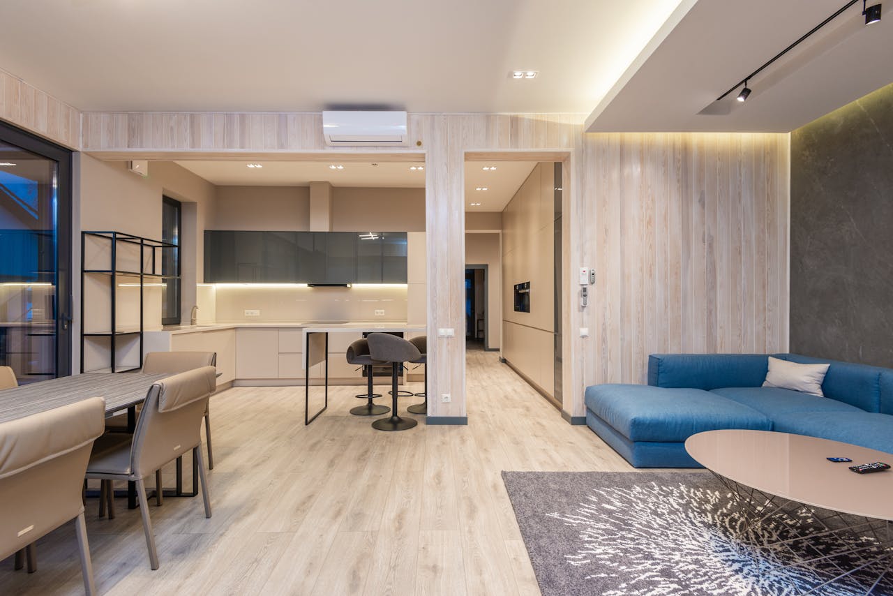 Interior of spacious modern studio apartment with comfortable blue corner sofa placed in front of dining table with chairs near kitchen zone